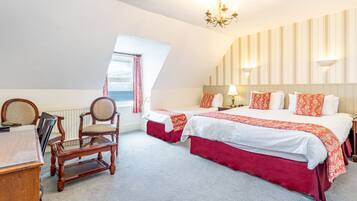 Een hotelkamer met twee bedden, een bureau, een stoel, een kroonluchter en een raam met gordijnen.