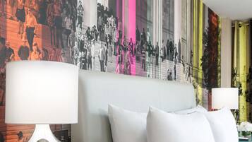 A hotel room with a large wall mural, a bed with white bedding, and two bedside lamps.