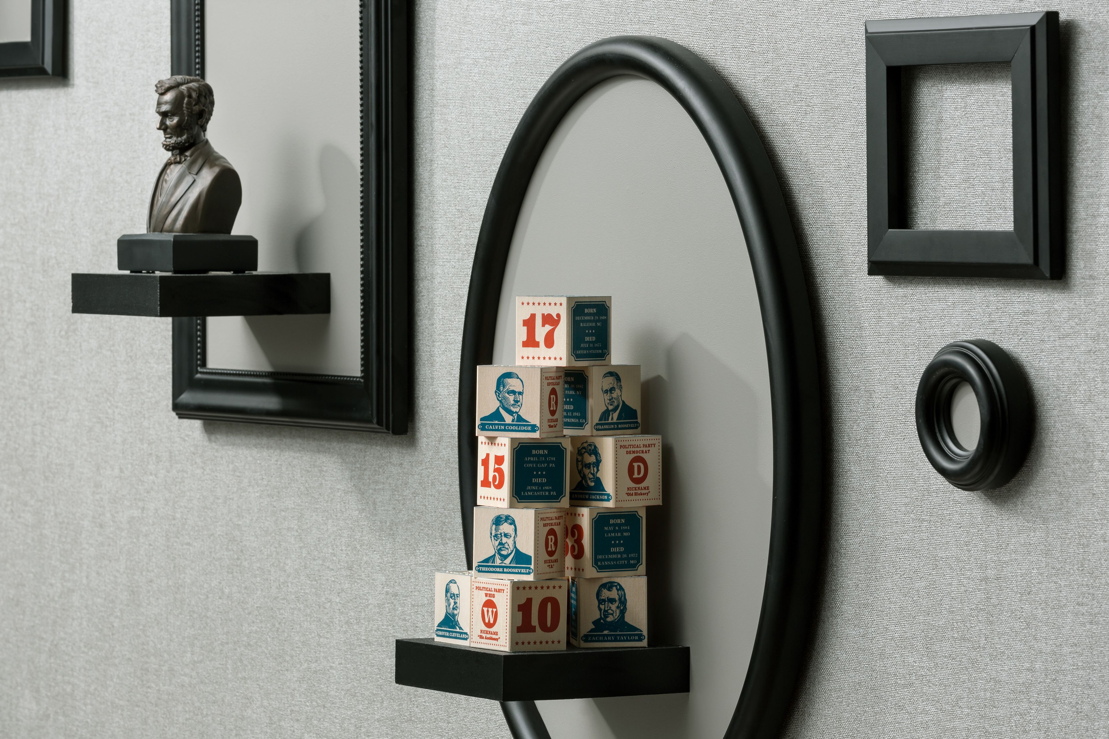 A wall with framed pictures, a bust sculpture, and a stack of numbered boxes.
