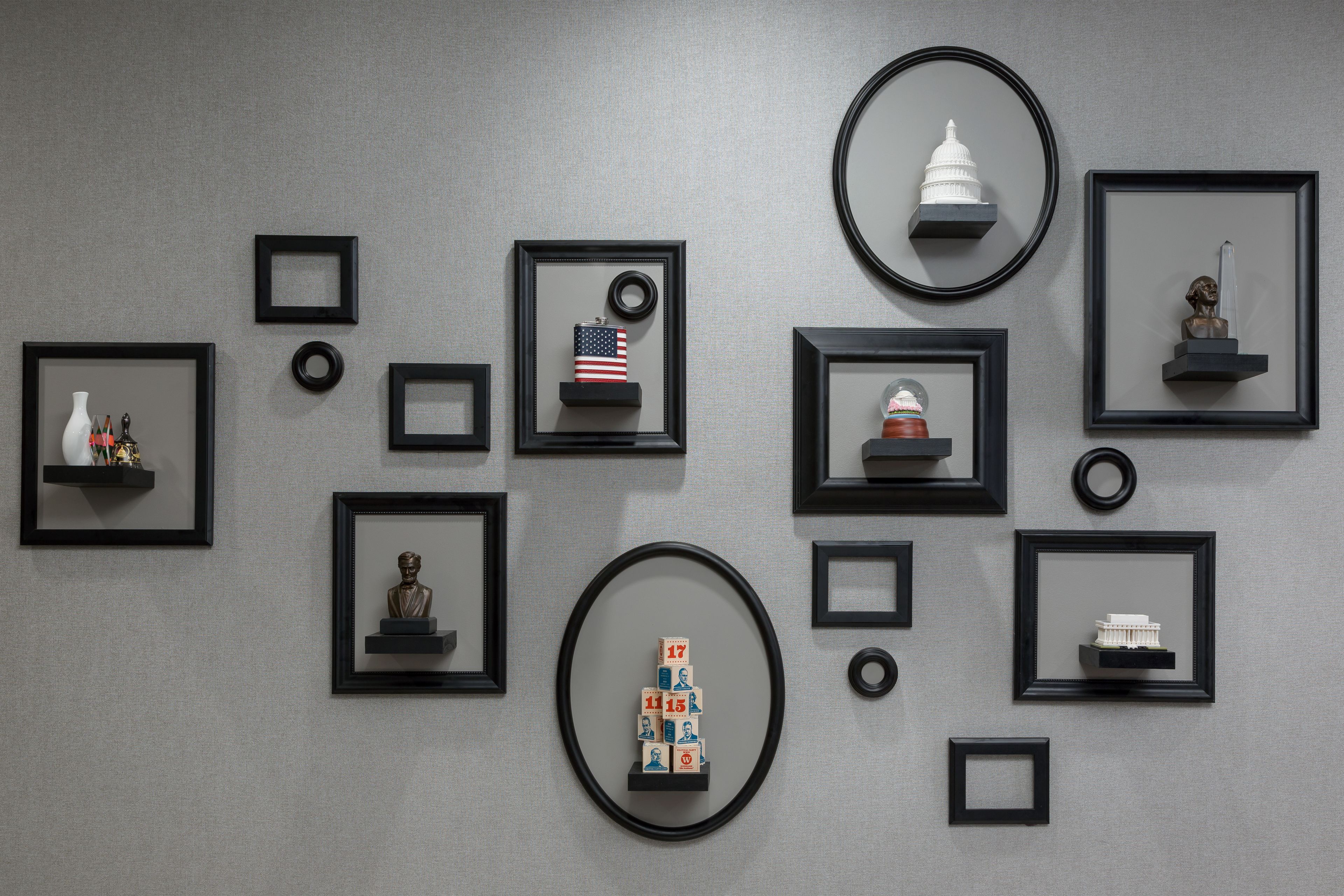 A wall with various framed artworks and sculptures, including a bust, a small American flag, and a model of a building.
