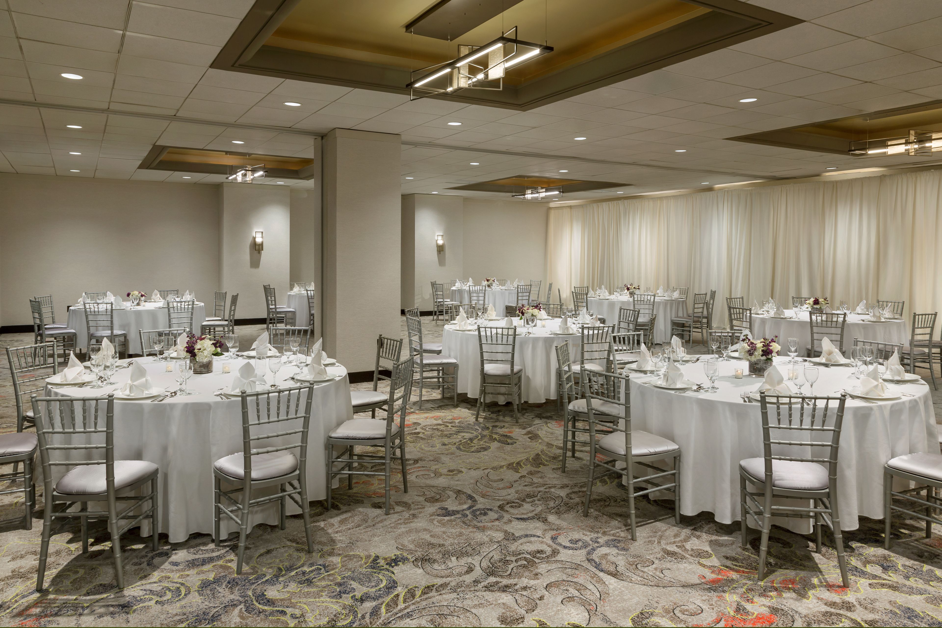 A banquet hall with round tables, white tablecloths, and grey chairs.
