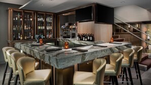 Zona de bar con mostrador de mármol, taburetes de cuero y una variedad de botellas de licores.