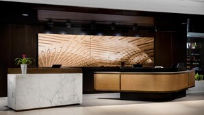Una recepción con mostrador de base de mármol y diseño de panel de madera, una planta en maceta y un techo moderno con listones de madera.