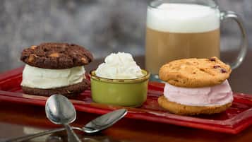 A tray with two ice cream sandwiches, a mug of coffee, and a small bowl of whipped cream.