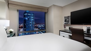 Una habitación de hotel con una cama grande, un escritorio, una silla, un televisor y una ventana con vista a la ciudad.