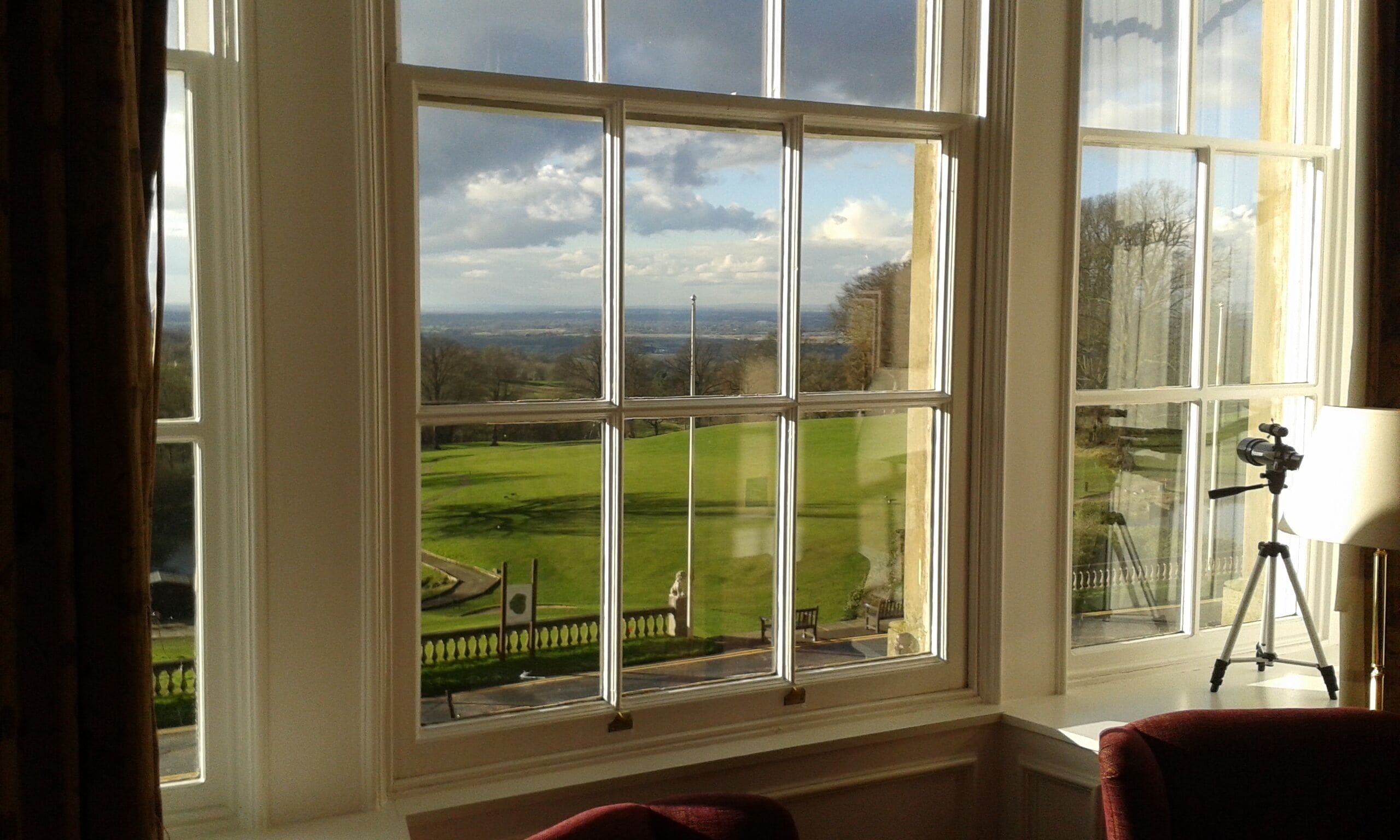 A room with a large window offering a view of a green landscape and a distant cityscape.