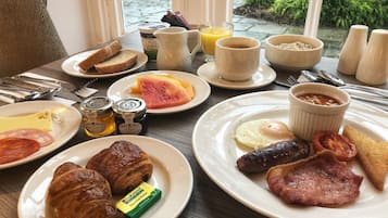 A breakfast table with croissants, ham, eggs, toast, jam, and a view of greenery outside.