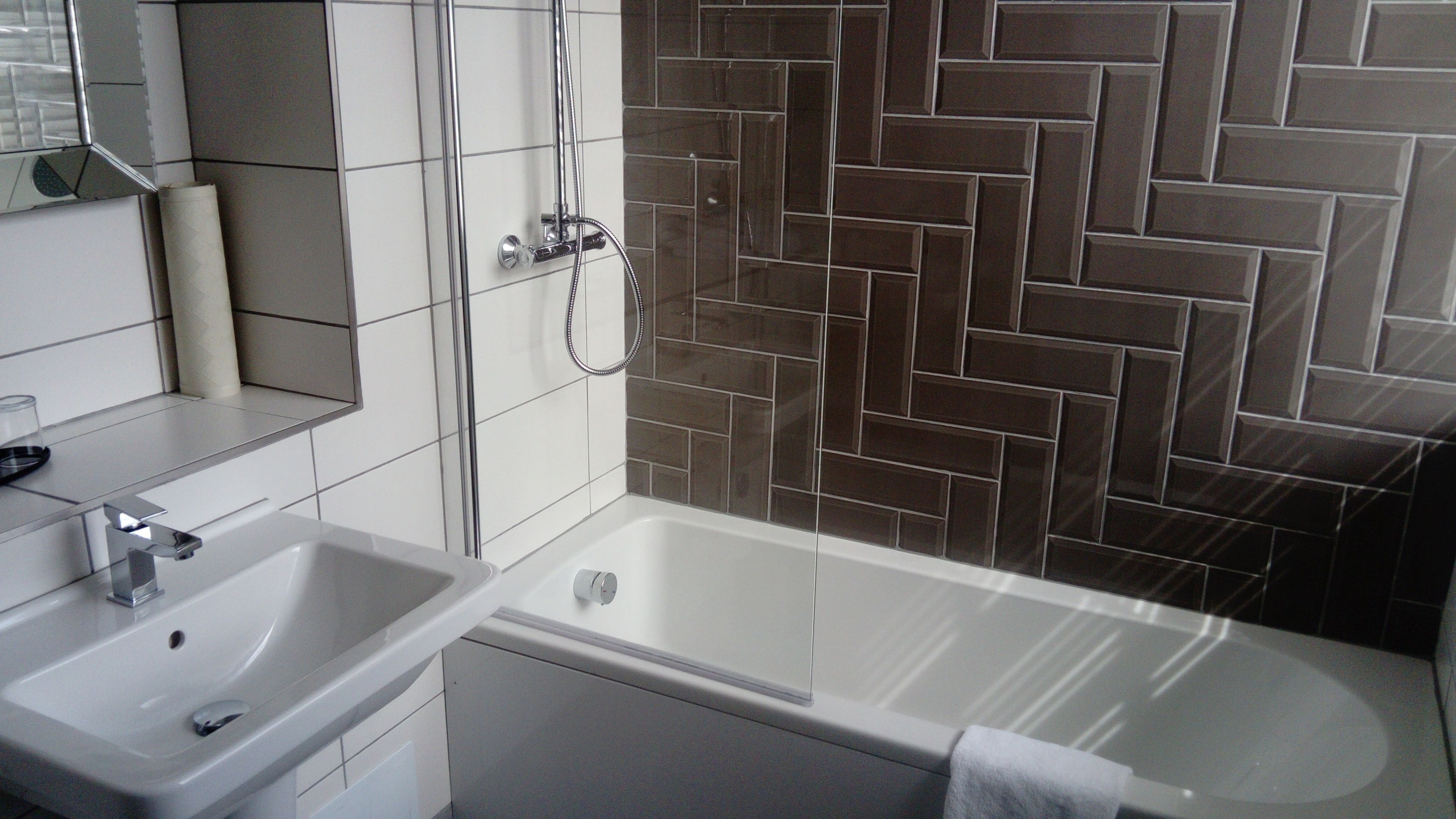 Een moderne badkamer met een witte wastafel, een bad en een douche met een zichtbare wand van visgraat tegels.