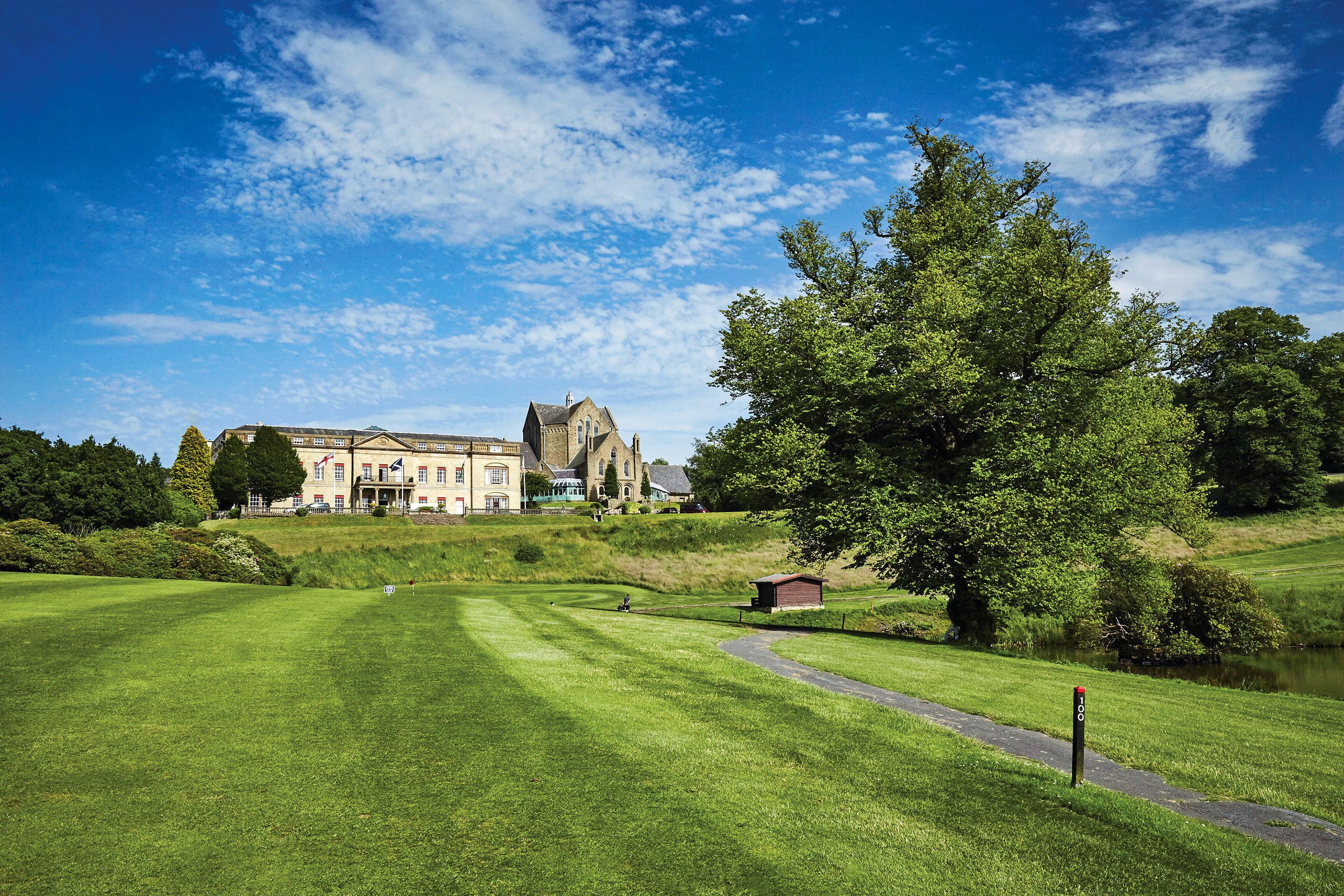 Ein Golfplatz mit Clubhaus, Teich und einer großen Baum.
