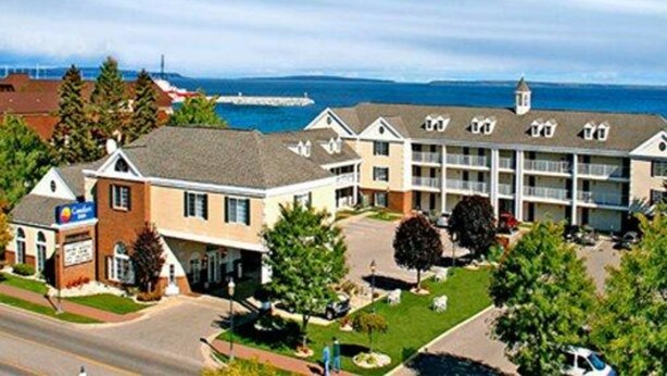 A hotel with a central building and a smaller annex, surrounded by greenery and a clear view of the sea. - Comfort Inn Lakeside (Mackinaw City)