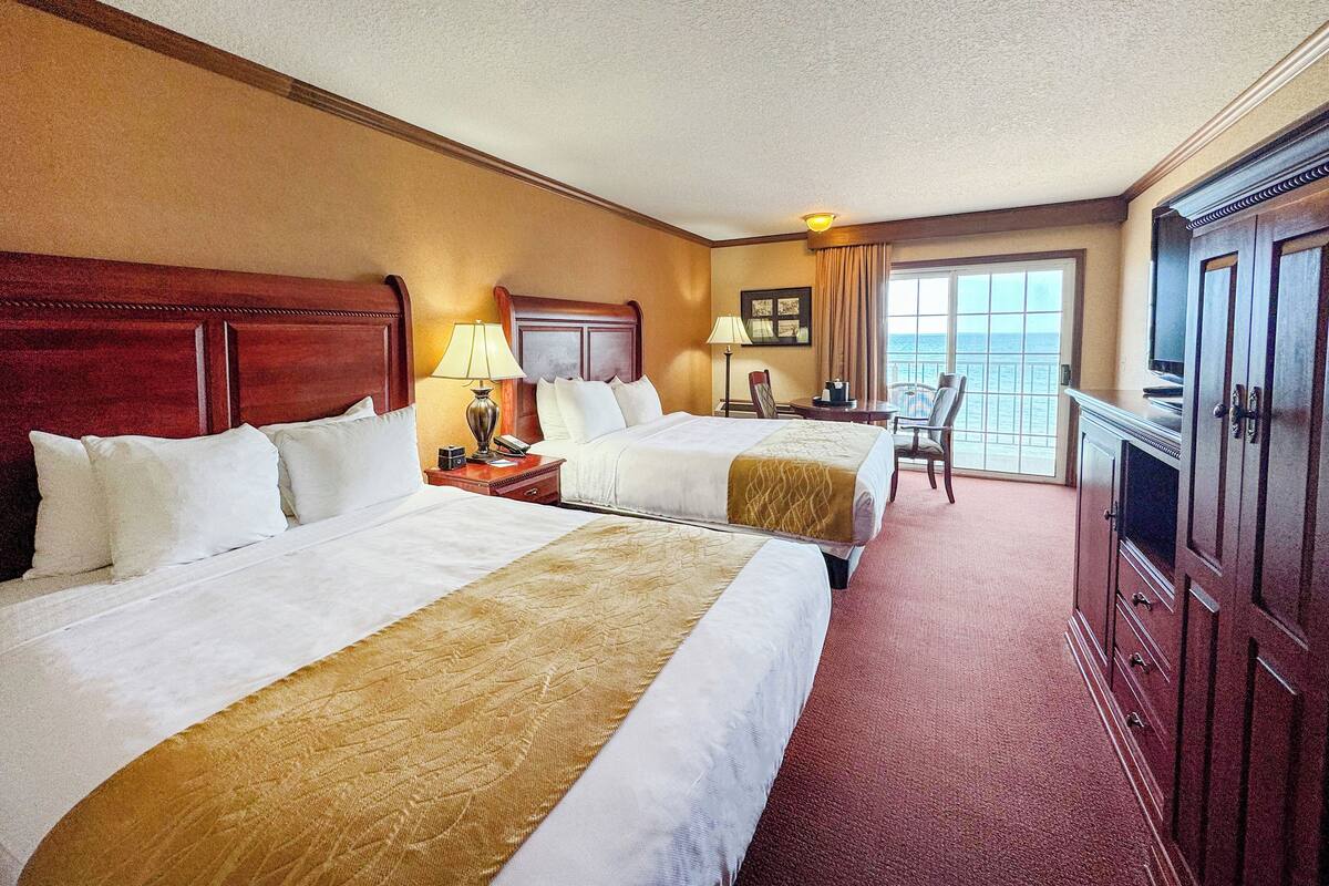 A hotel room with two beds, a desk, a chair, and a television.
