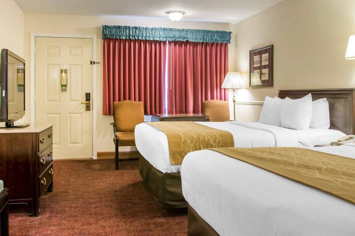 A hotel room with two beds, a desk, a chair, a TV, and a door.