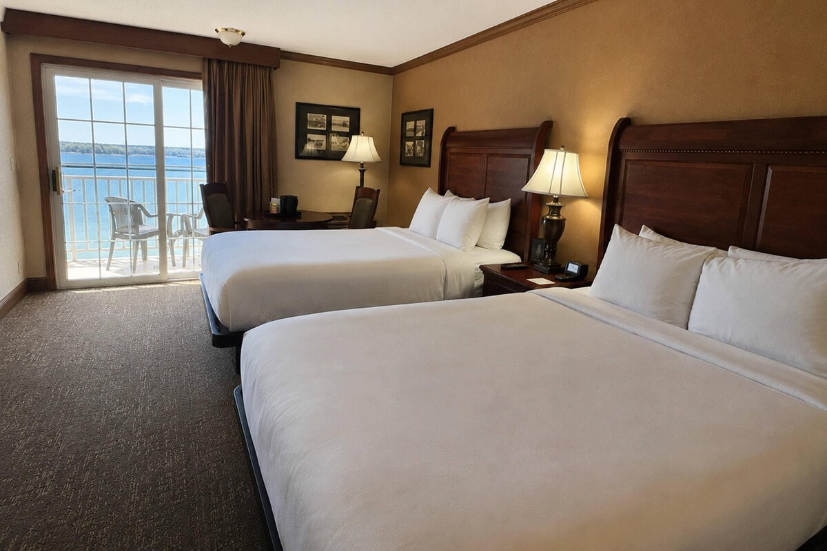 A hotel room with two beds, a desk, a chair, and a view of the sea.