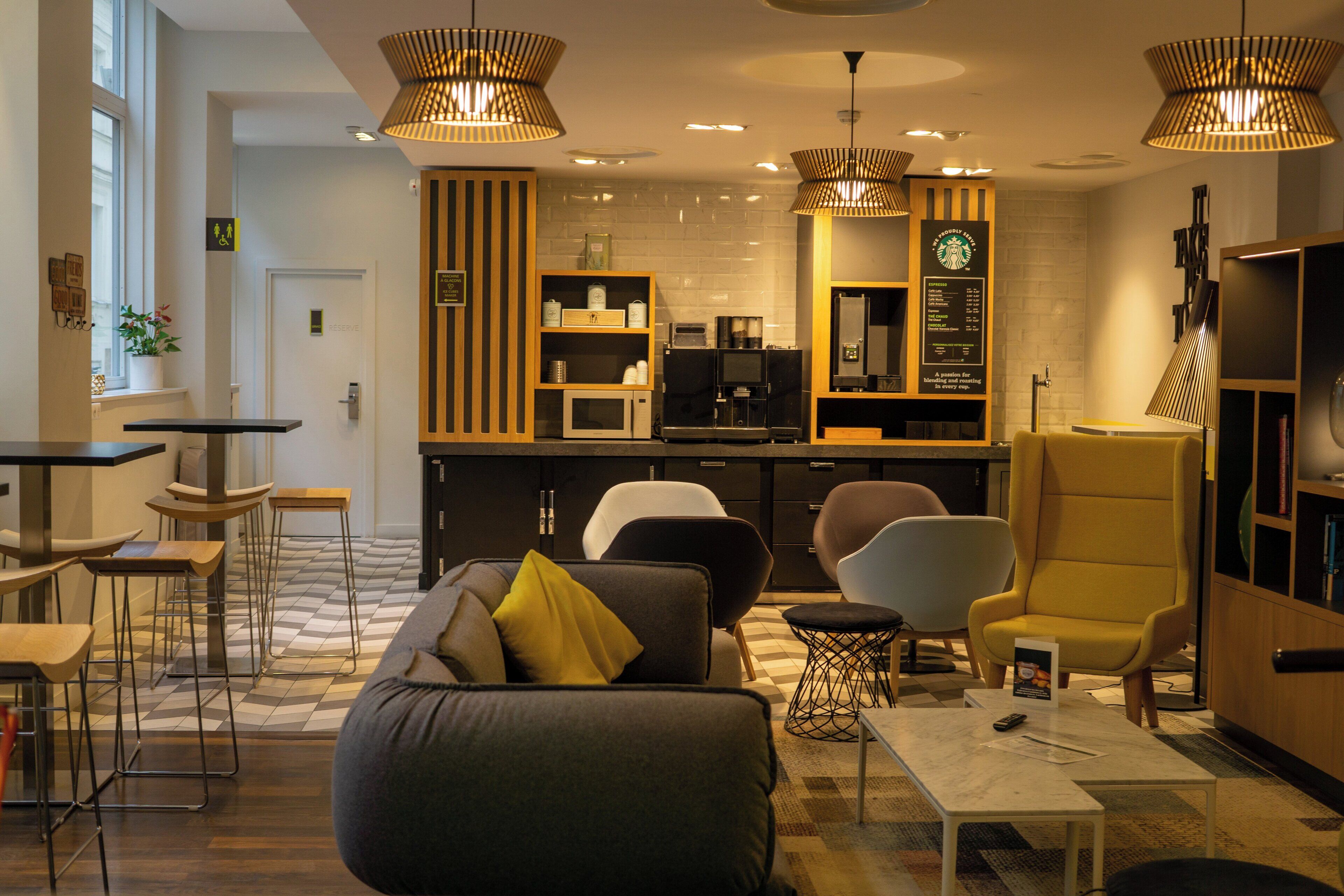 Un intérieur moderne avec un canapé, des fauteuils, une machine à café et un panneau affichant le menu.