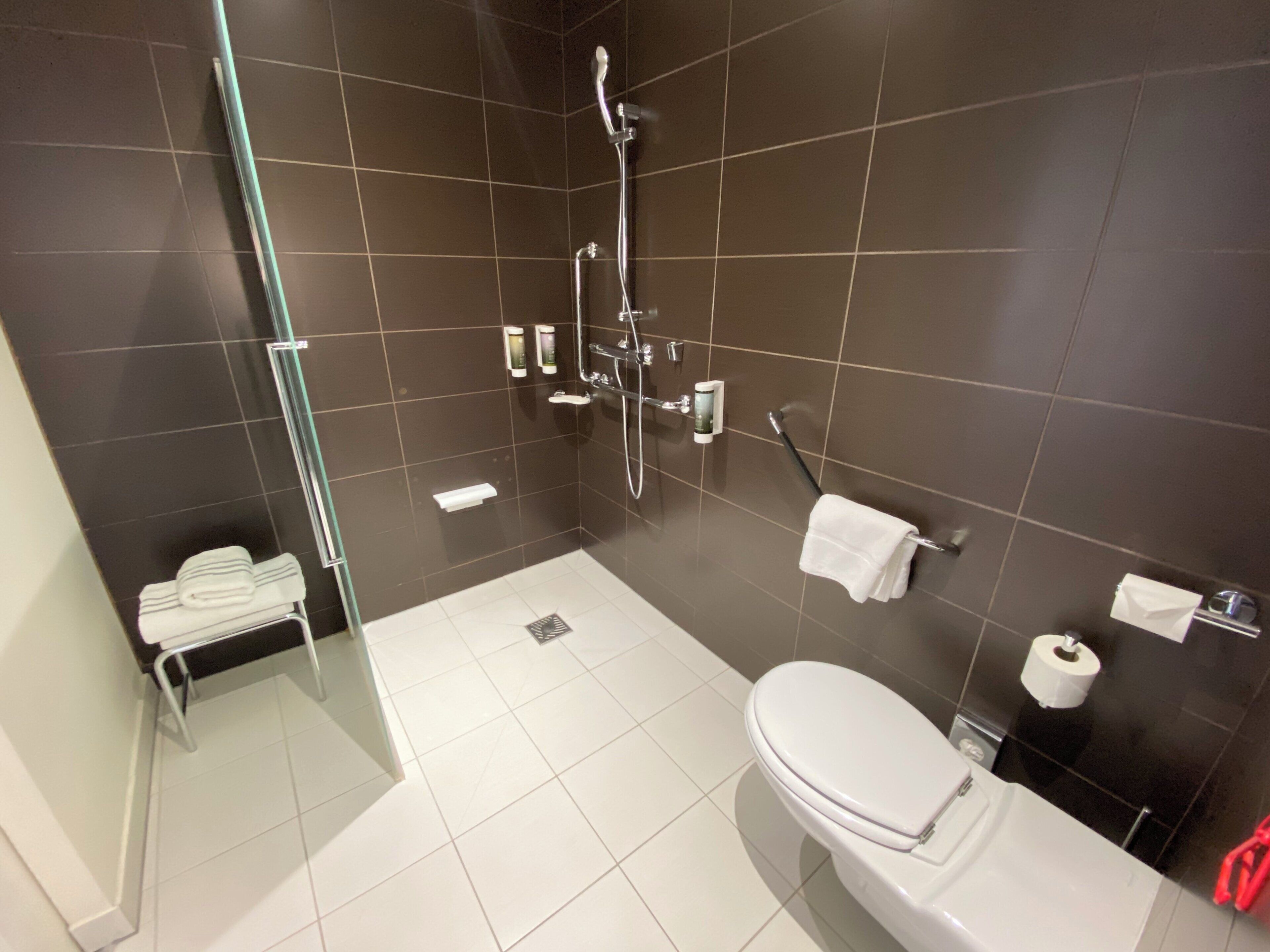 A modern bathroom with a shower, toilet, and towel rack.