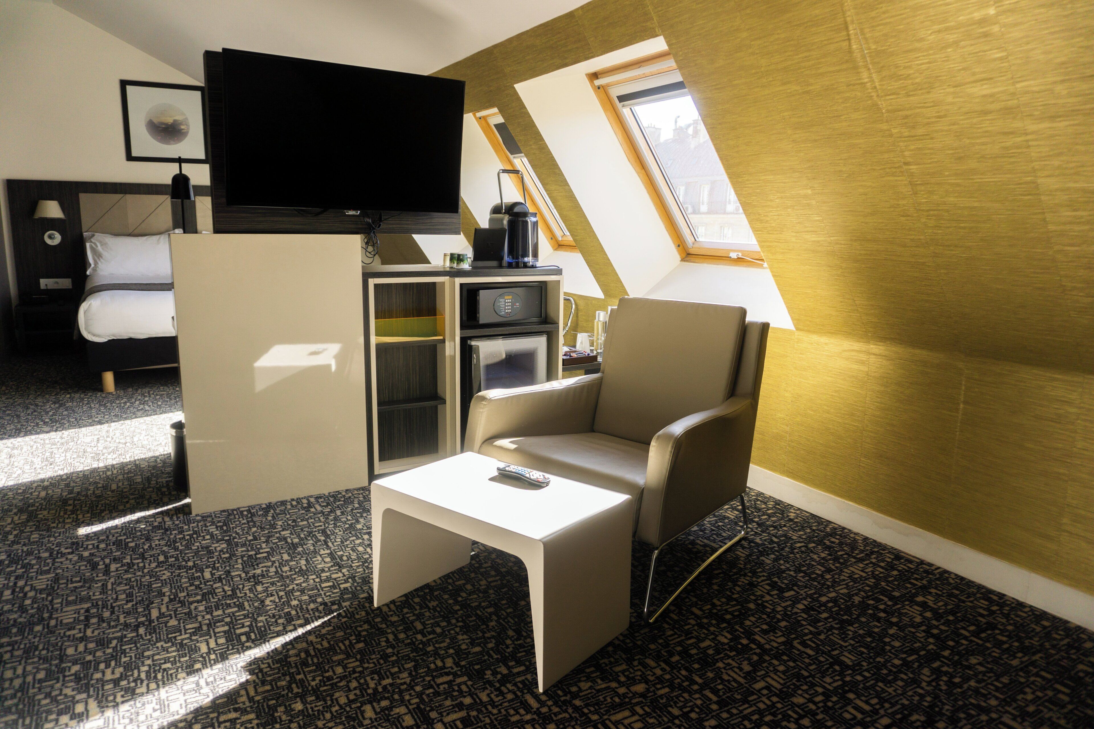 A hotel room with a bed, a television, a small kitchenette, a sofa, and a window with a view.