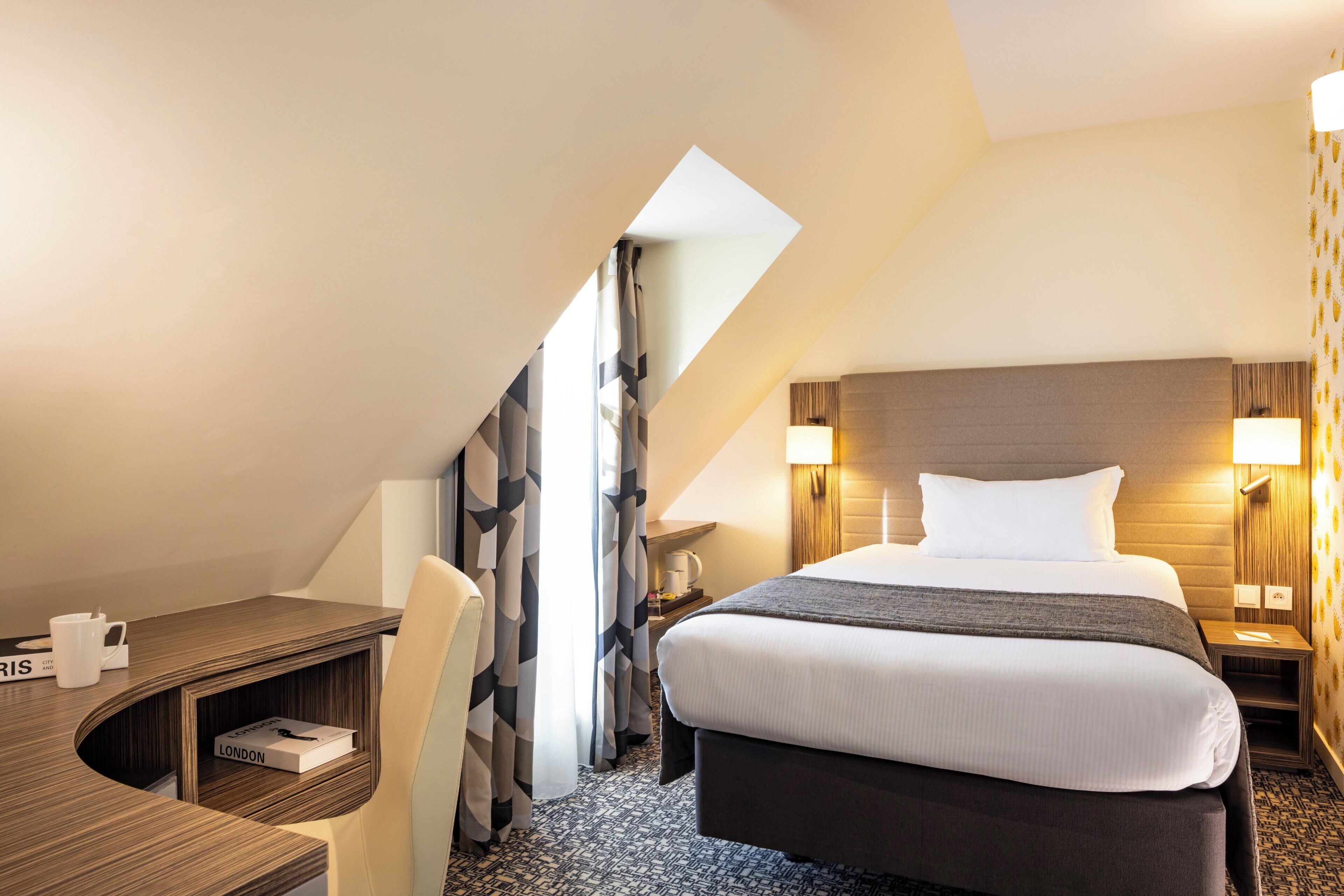 Habitación de hotel con cama, escritorio, silla y una pequeña mesa con un libro titulado 'LONDON'.