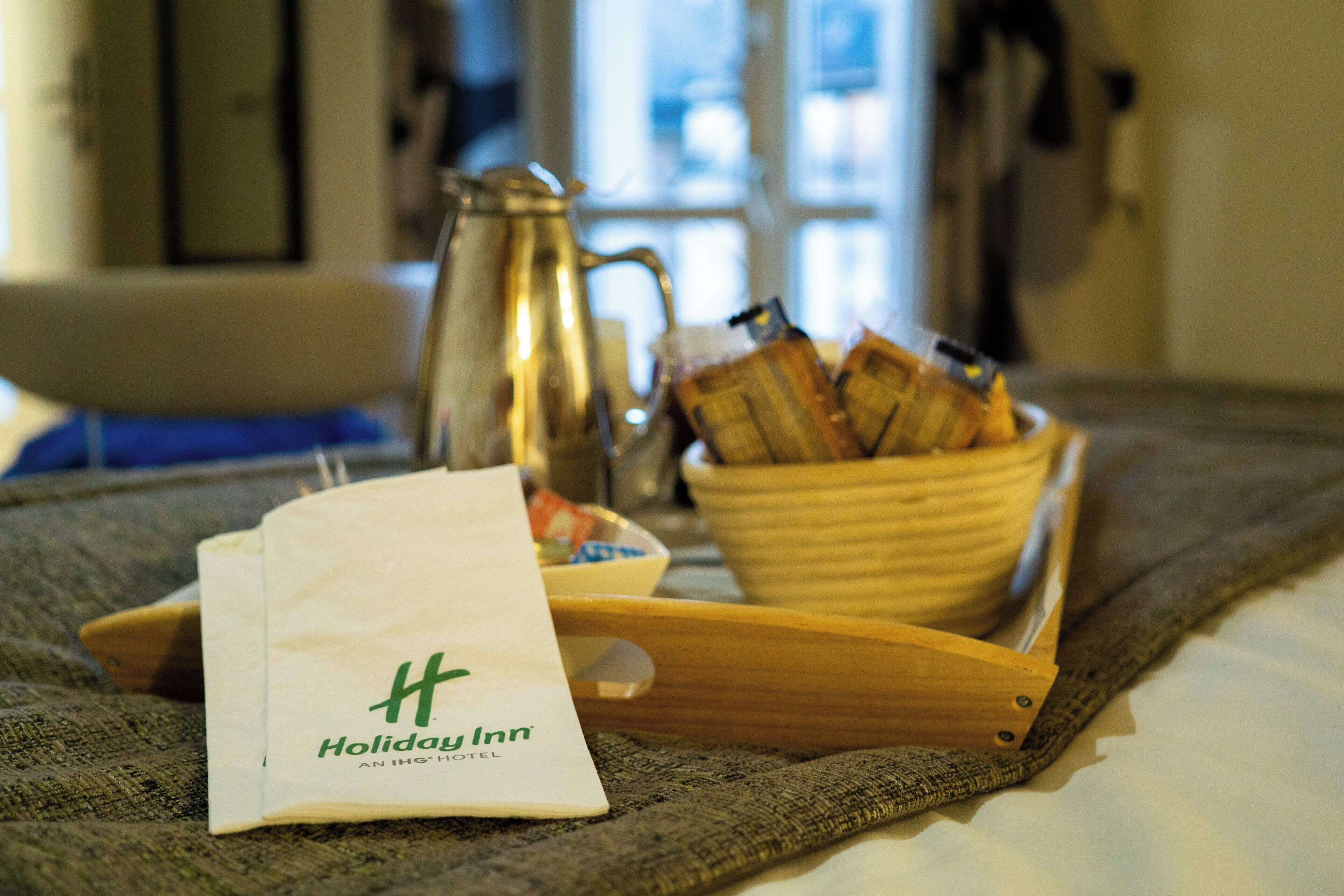 Un plateau avec un sac du Holiday Inn, un bol de pain et une carafe, le tout posé sur un tapis texturé.