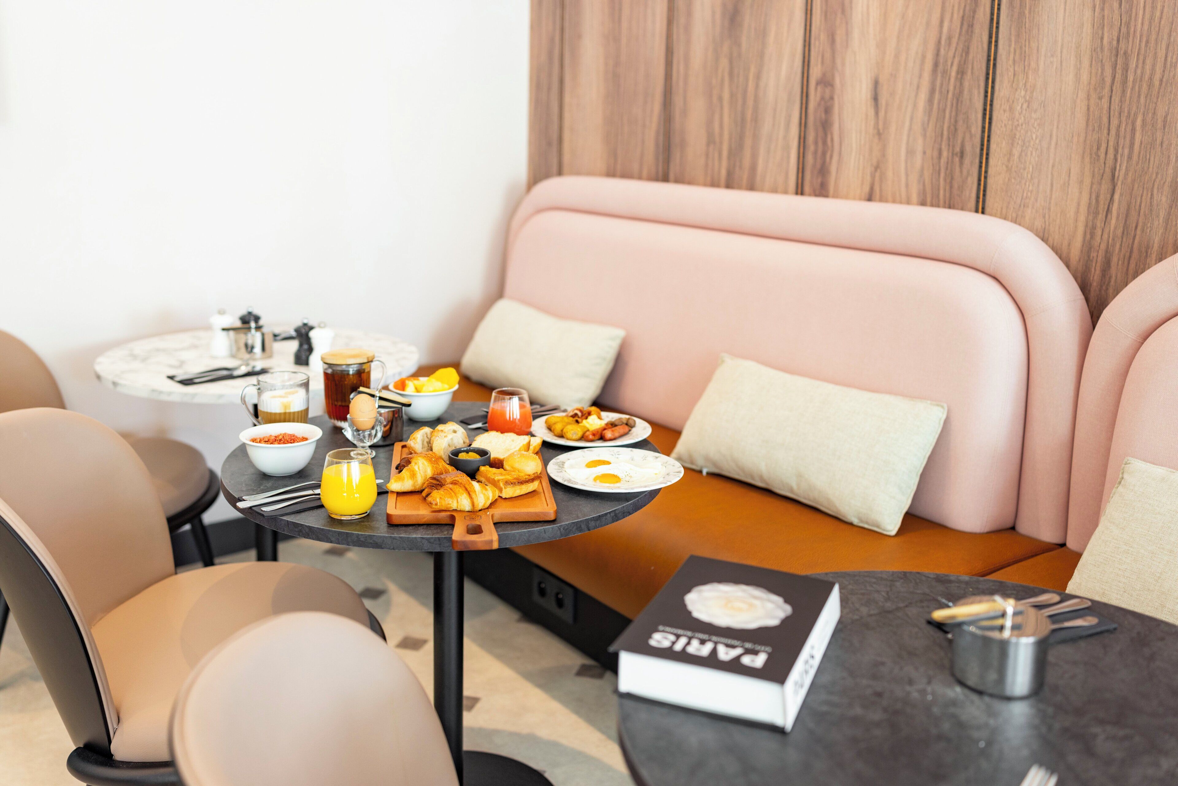 A modern living room with a sofa, a dining table with breakfast, and a book titled 'PARIS'.