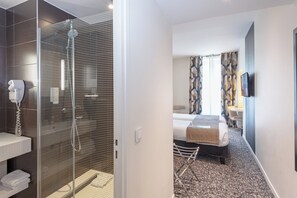 A hotel room with a shower, a bed, a TV, and a bathroom with a towel rack and a hairdryer. - Holiday Inn Paris Opéra Grands Boulevards by IHG (Paris)