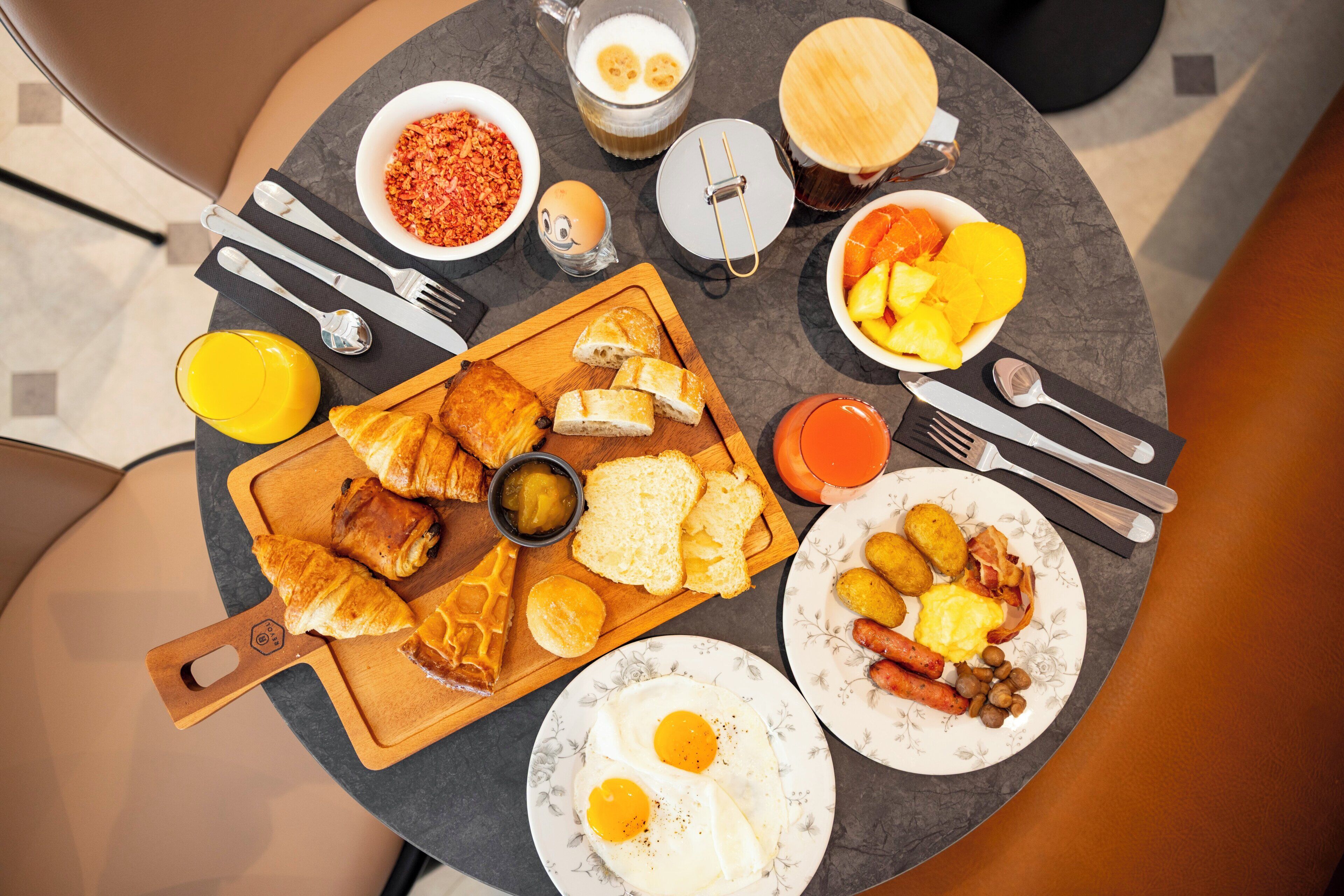 A breakfast table with croissants, eggs, sausages, and various fruits.