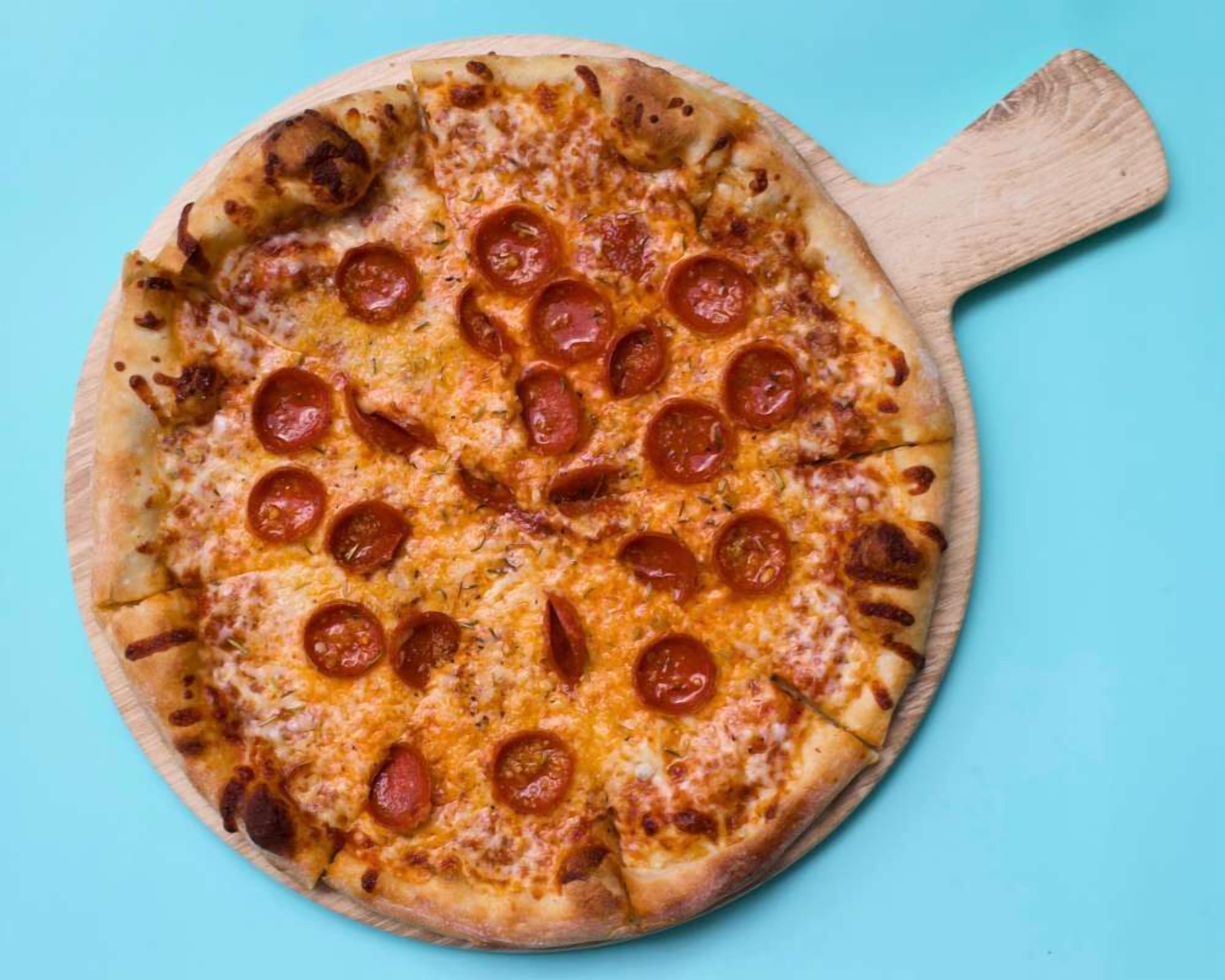 A pizza with pepperoni slices on a wooden board against a blue background.