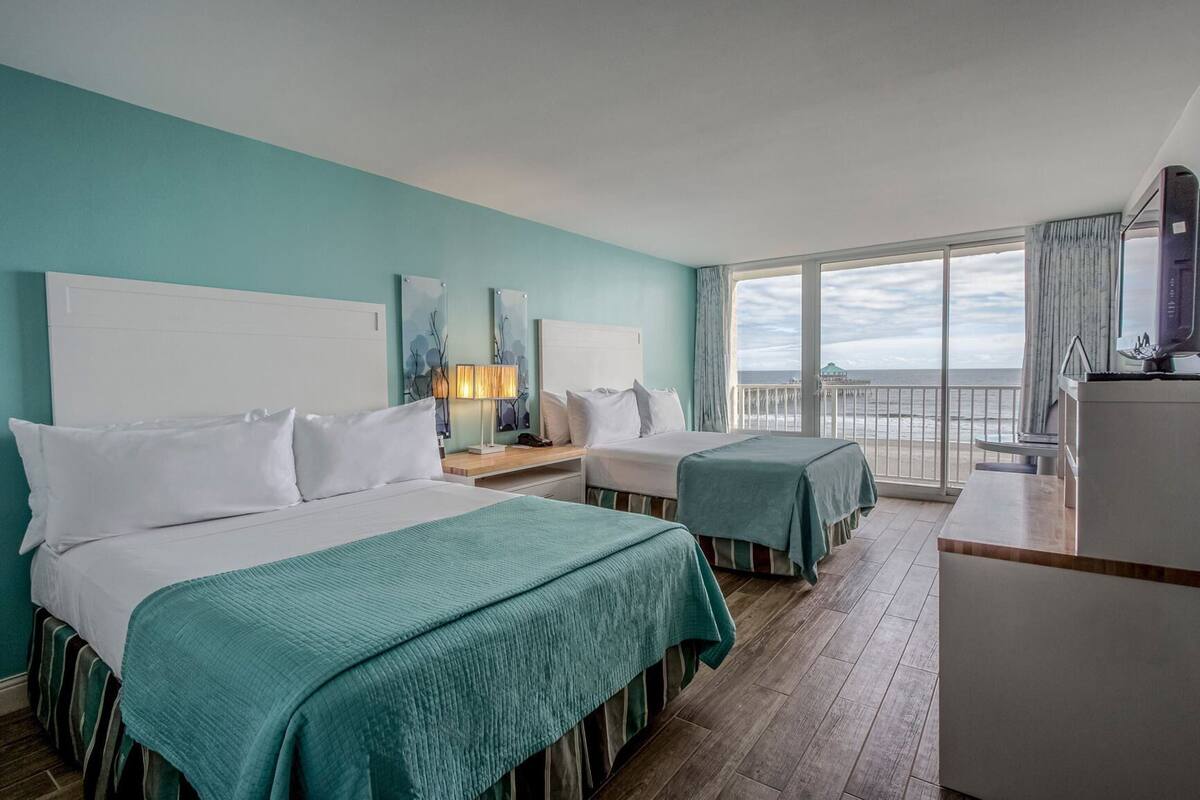 Une chambre d’hôtel avec deux lits, un bureau, une chaise, une télévision et un balcon avec vue sur la mer.
