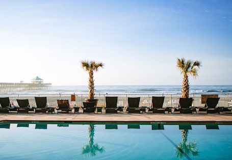 A poolside area with lounge chairs and palm trees, overlooking the ocean.