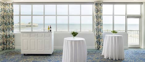 A room with large windows, a white reception desk, and two round tables with white tablecloths.