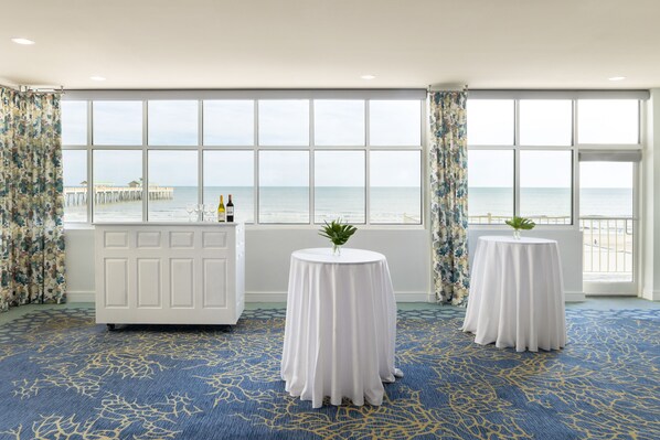 A room with large windows, a white reception desk, and two round tables with white tablecloths. - Tides Folly Beach, Charleston's Oceanfront Hotel (Folly Beach)