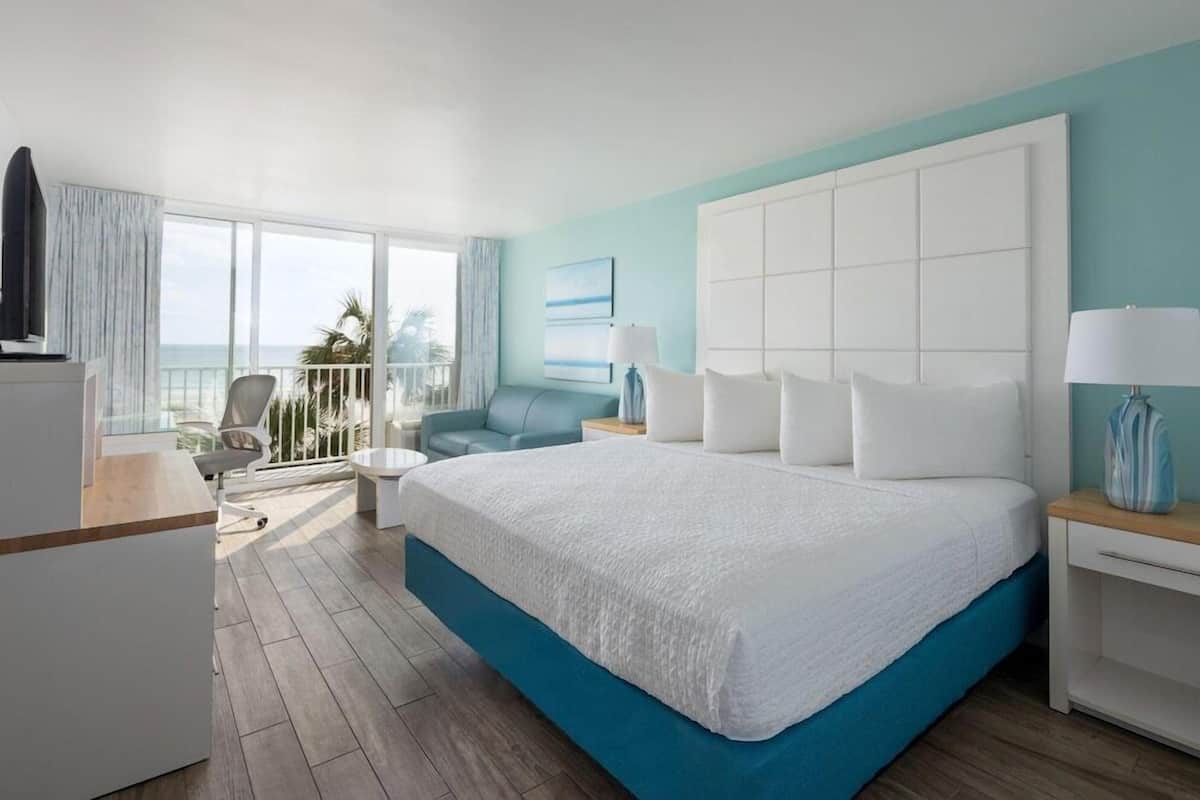 Une chambre d’hôtel avec un grand lit, un bureau, une chaise, un balcon avec vue et une télévision.
