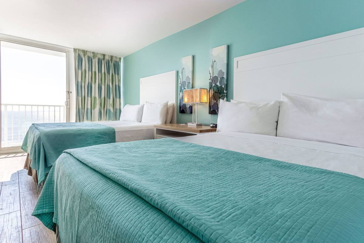 Une chambre d’hôtel avec deux lits, un balcon et vue sur la mer.