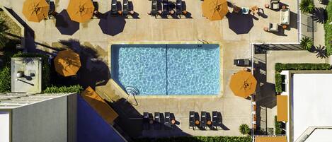 Vista aerea di una piscina sul tetto con lettini e ombrelloni, circondata dal verde.
