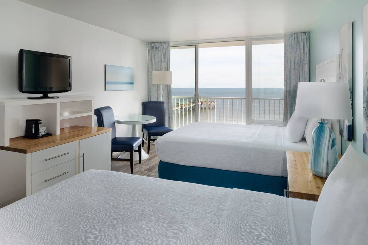 Une chambre d’hôtel avec deux lits, une télévision, un bureau avec une lampe et une vue sur l’océan.