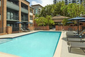Relax by the rectangular pool surrounded by lounge chairs and umbrellas, with views of the surrounding area from the adjacent building's balconies.