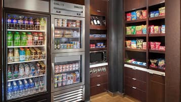 Zona autoservicio de bebidas y aperitivos con varios dispensadores, microondas y estantes con snacks.