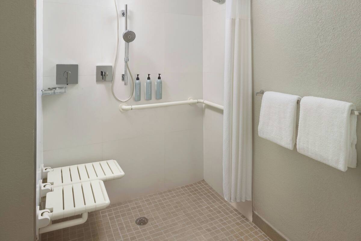 A small, enclosed shower area with a white toilet, grab bars, and a showerhead.