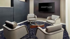 A modern room with a dark wall, a flat-screen TV, and three grey armchairs around a glass coffee table. - Courtyard® by Marriott® Fort Lauderdale City of Plantation (Plantation)