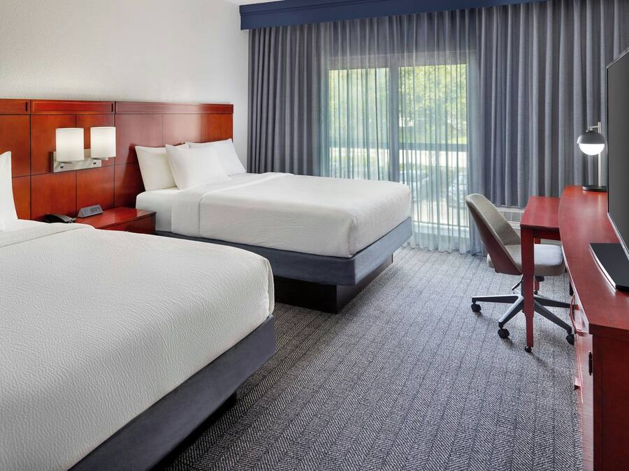 A hotel room with two beds, a desk, a TV, and a window with curtains.