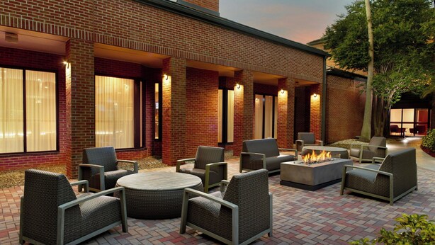 An outdoor patio with wicker furniture, a fire pit, and a brick building with large windows. - Courtyard® by Marriott® Fort Lauderdale City of Plantation (Plantation)
