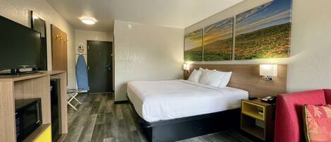 A hotel room with a bed, a TV, a desk, and a red chair.