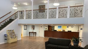 Eine geräumige Lobby mit einem hölzernen Empfangstresen, gestreiften Sofas, einer Treppe mit schmiedeeisernen Geländern und einem Aushangbrett mit Broschüren.