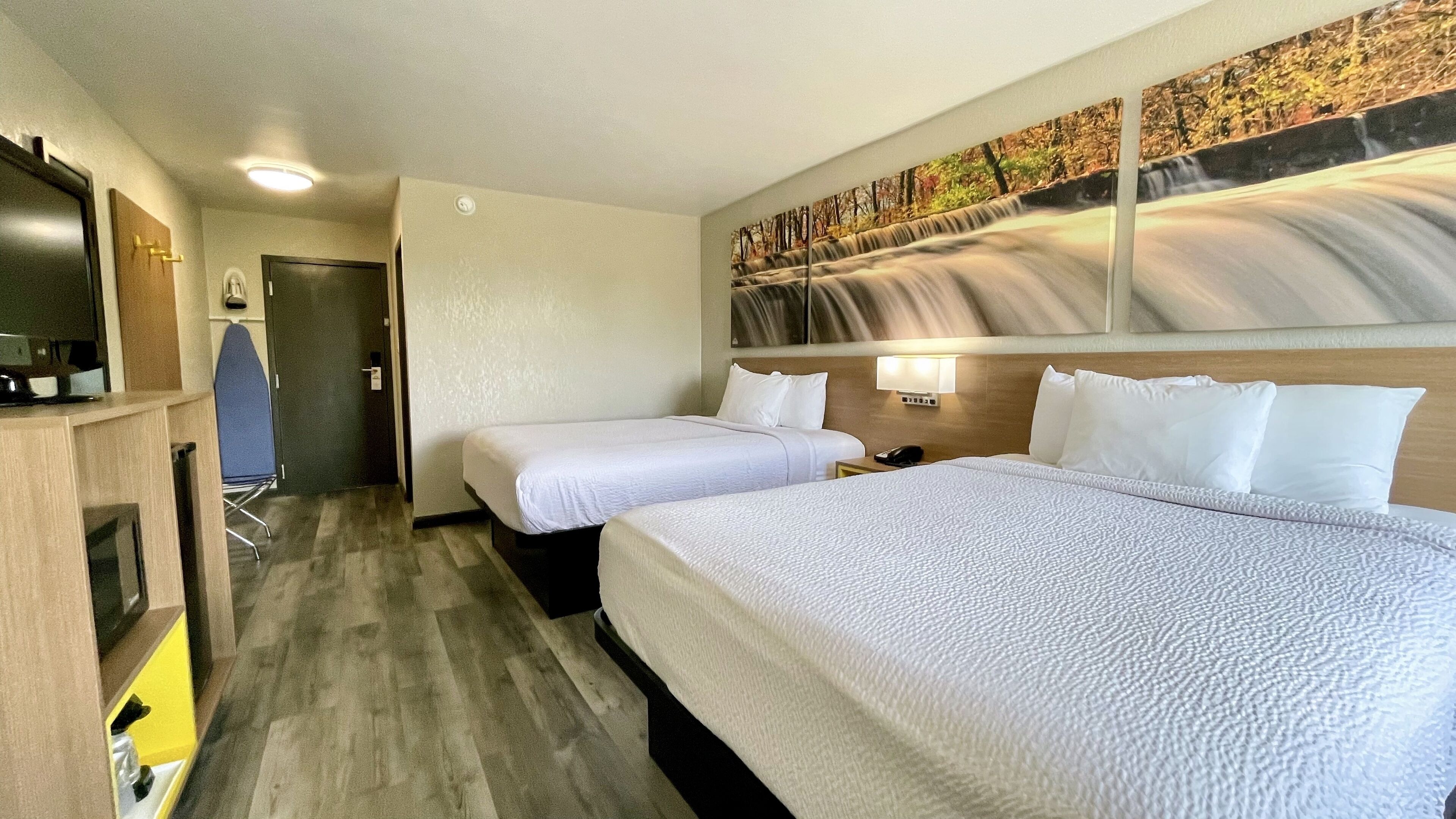 A hotel room with two beds, a TV, a desk, and a painting on the wall.