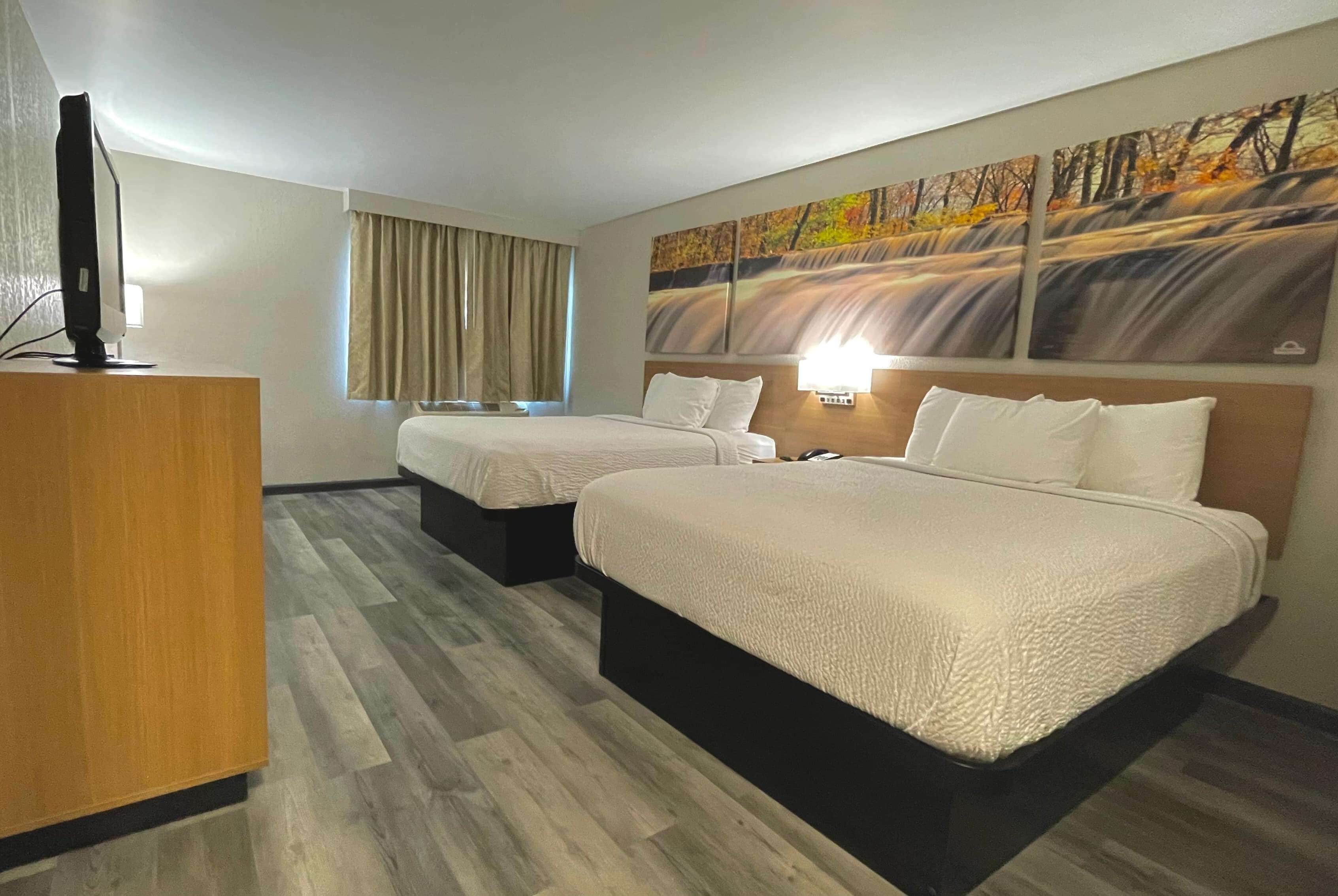 Una habitación de hotel con dos camas, un escritorio, un televisor y un cuadro en la pared.
