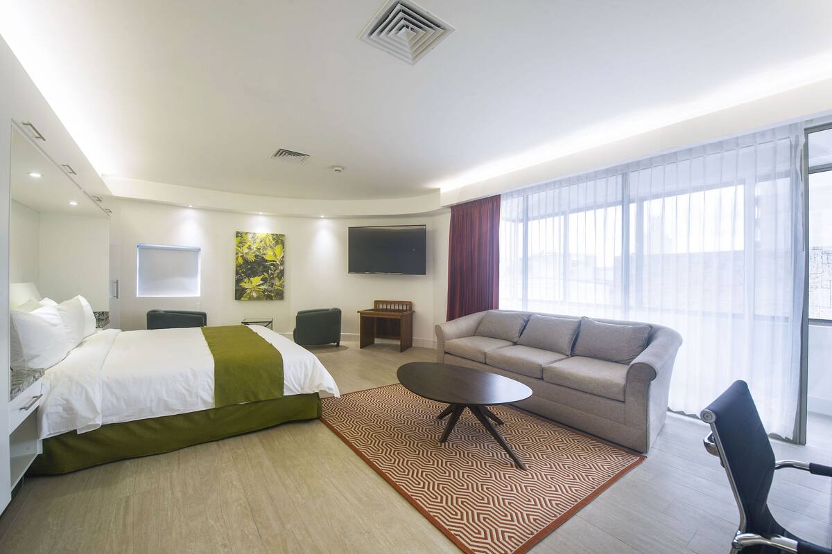 A modern hotel room with a bed, sofa, and a TV.