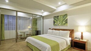 A hotel room with a bed, a bedside table with a lamp, a chair, a small table, and a sliding glass door leading to a balcony. - Balmoral Hotel San José CR, Historic District (San José)