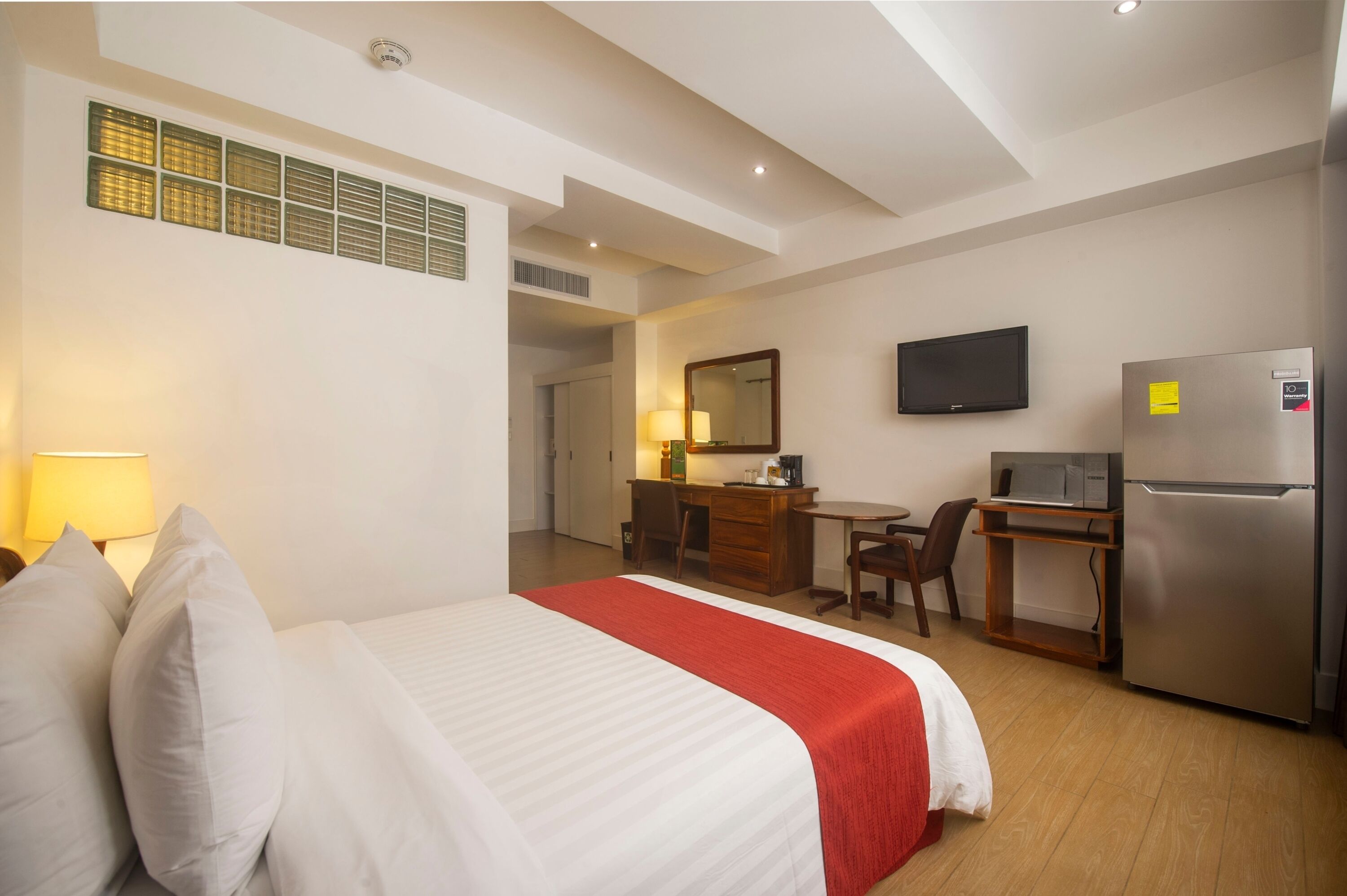 A hotel room with a bed, desk, chair, television, and refrigerator.