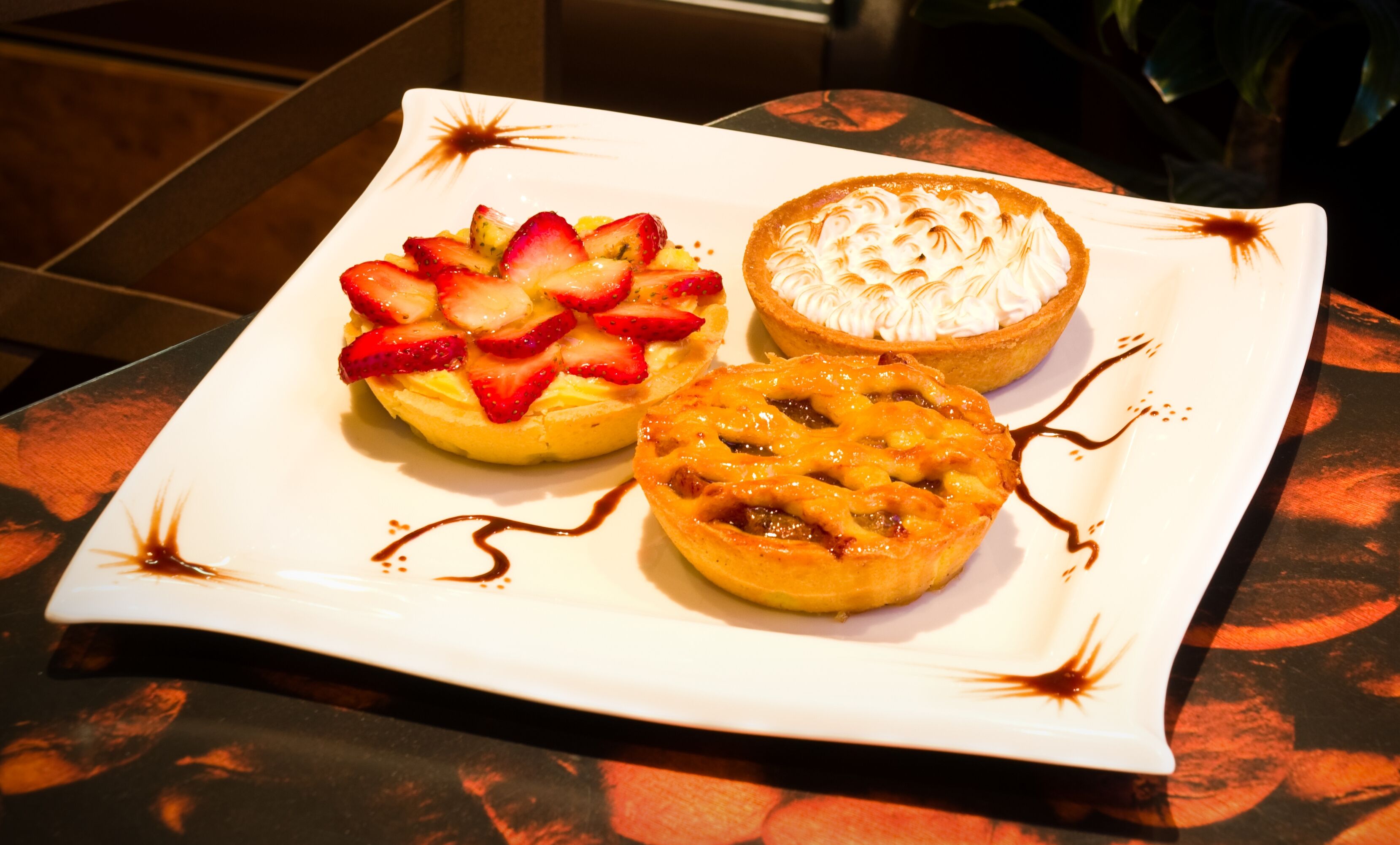 Un plato blanco rectangular con tres pasteles: uno cubierto de fresas, uno con glaseado blanco y uno con fruta.