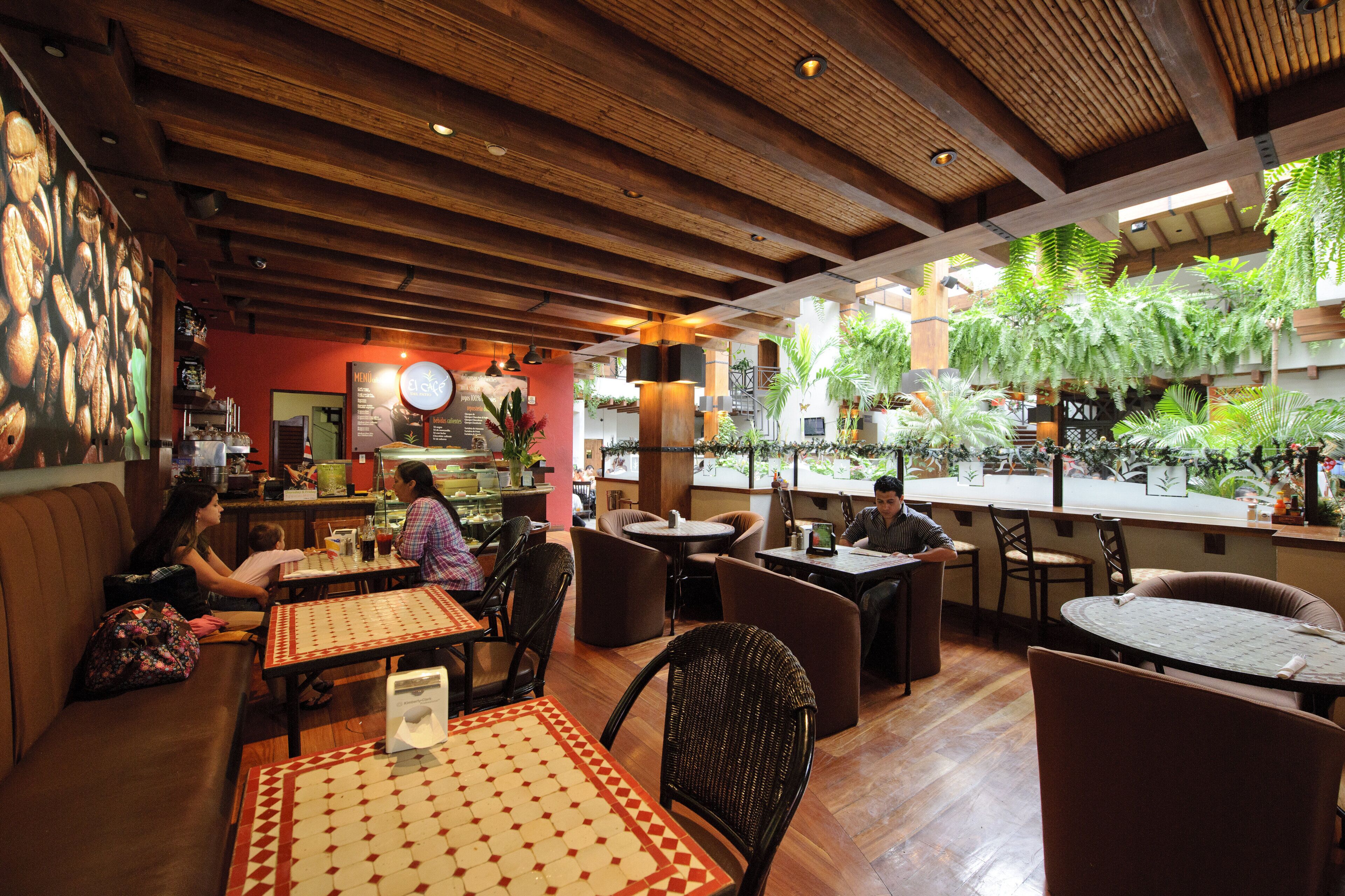 An indoor restaurant with wooden ceilings, tables, and chairs, and a view of greenery outside.