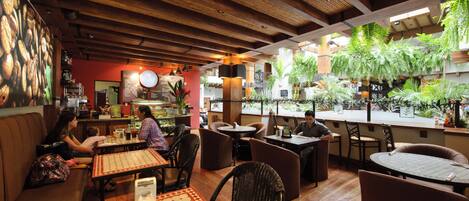 An indoor restaurant with wooden ceilings, tables, and chairs, and a view of greenery outside.